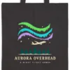 Close-up of the Aurora Overhead design printed in warm cream ink on a black canvas tote, with the top seam and handles