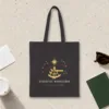 Celestial Navigation design in warm cream ink on a black canvas tote, laid flat on a light terrazzo terminal floor