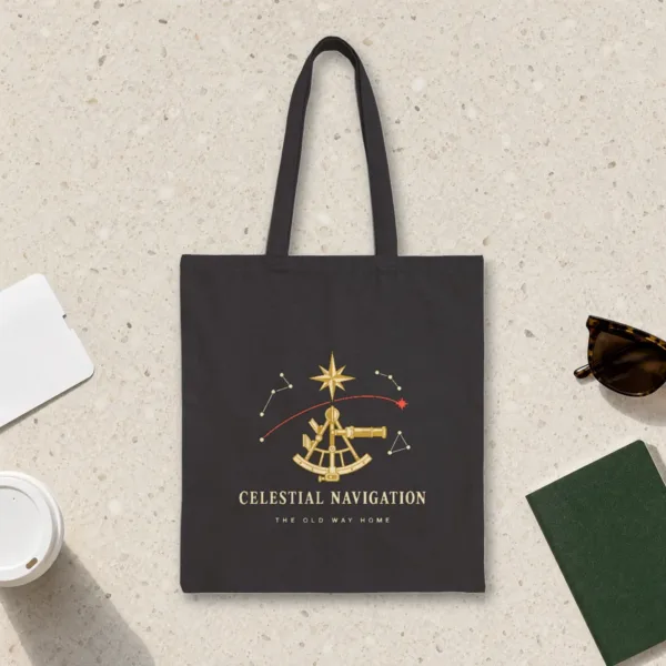 Celestial Navigation design in warm cream ink on a black canvas tote, laid flat on a light terrazzo terminal floor