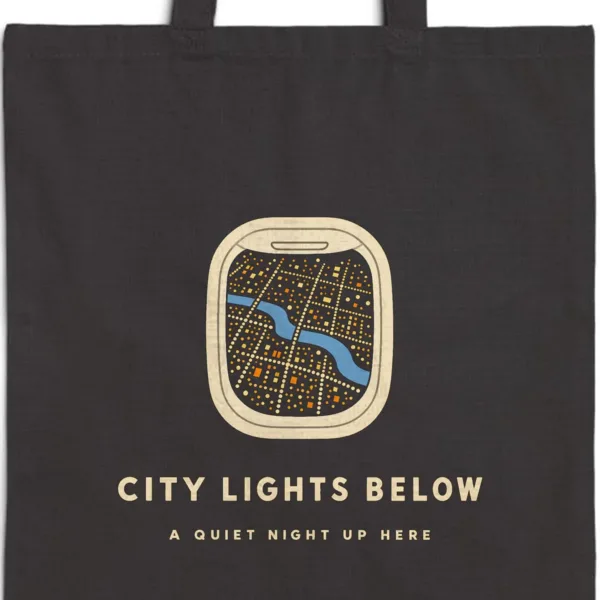 Close-up of the City Lights Below design printed in warm cream ink on a black canvas tote, with the top seam and handles