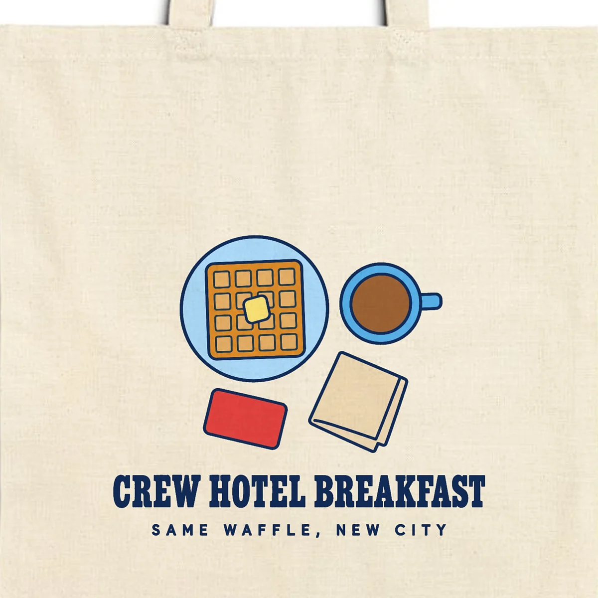 Close-up of the Crew Hotel Breakfast design printed in navy ink on a natural canvas tote, with the top seam and handles