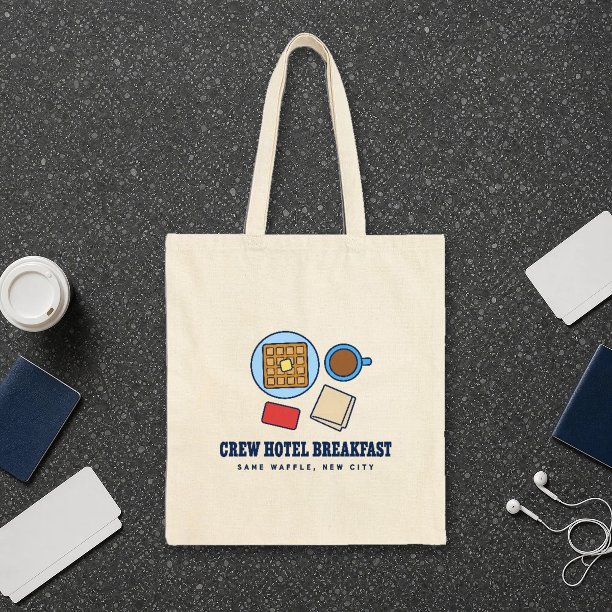 Crew Hotel Breakfast design in navy ink on a natural canvas tote, laid flat on a dark terrazzo terminal floor