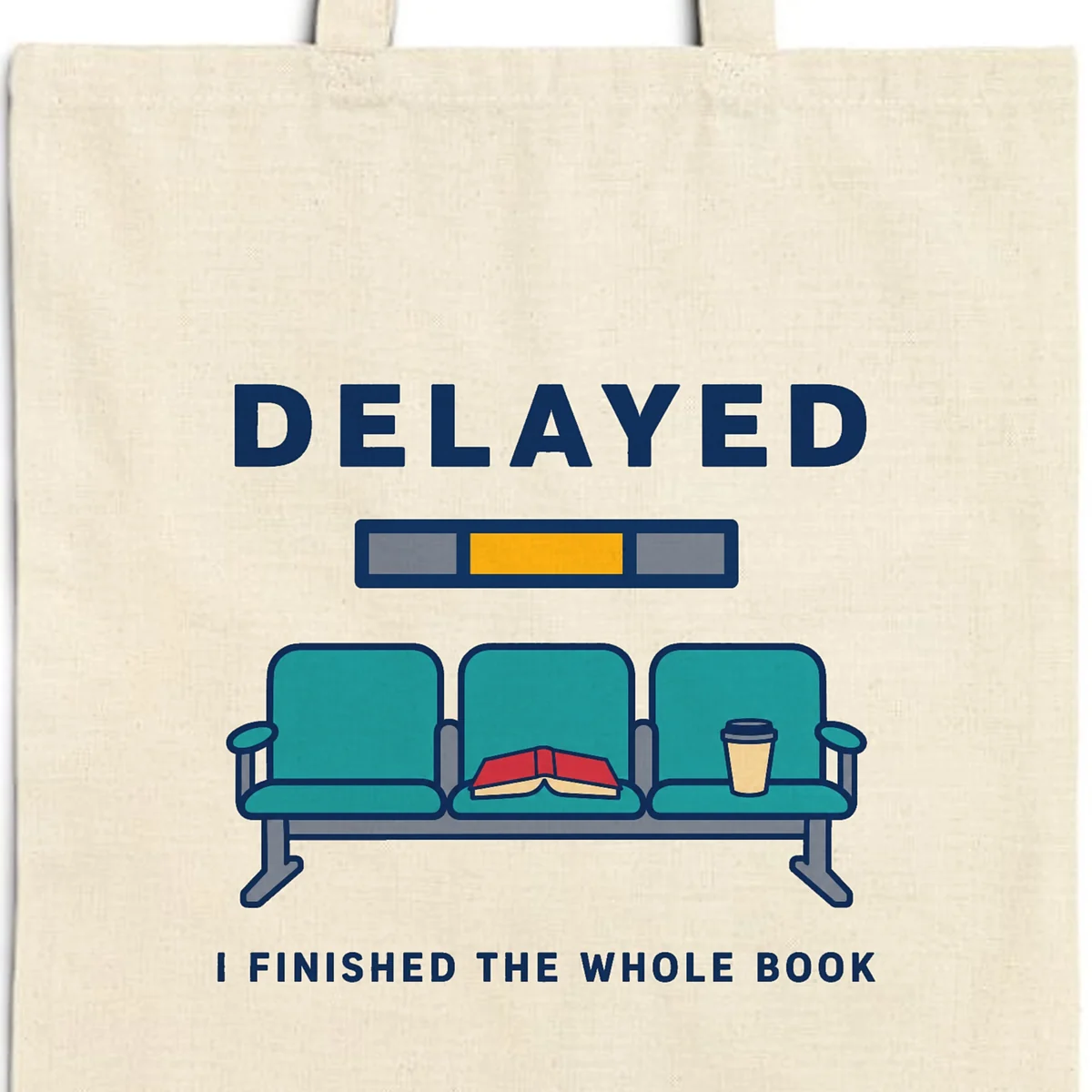 Close-up of the Delayed with a Book design printed in navy ink on a natural canvas tote, with the top seam and handles