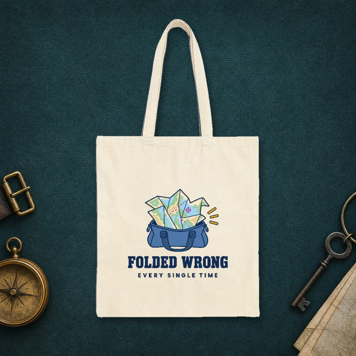 Folded Wrong design in navy ink on a natural canvas tote, laid flat on the leather lid of a travel trunk