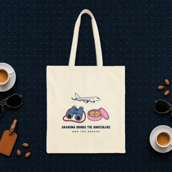 Grandma Brings the Binoculars design in navy ink on a natural canvas tote, laid flat on an airport lounge carpet