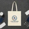 It Takes a Whole Airport design in navy ink on a natural canvas tote, laid flat on a dark terrazzo terminal floor