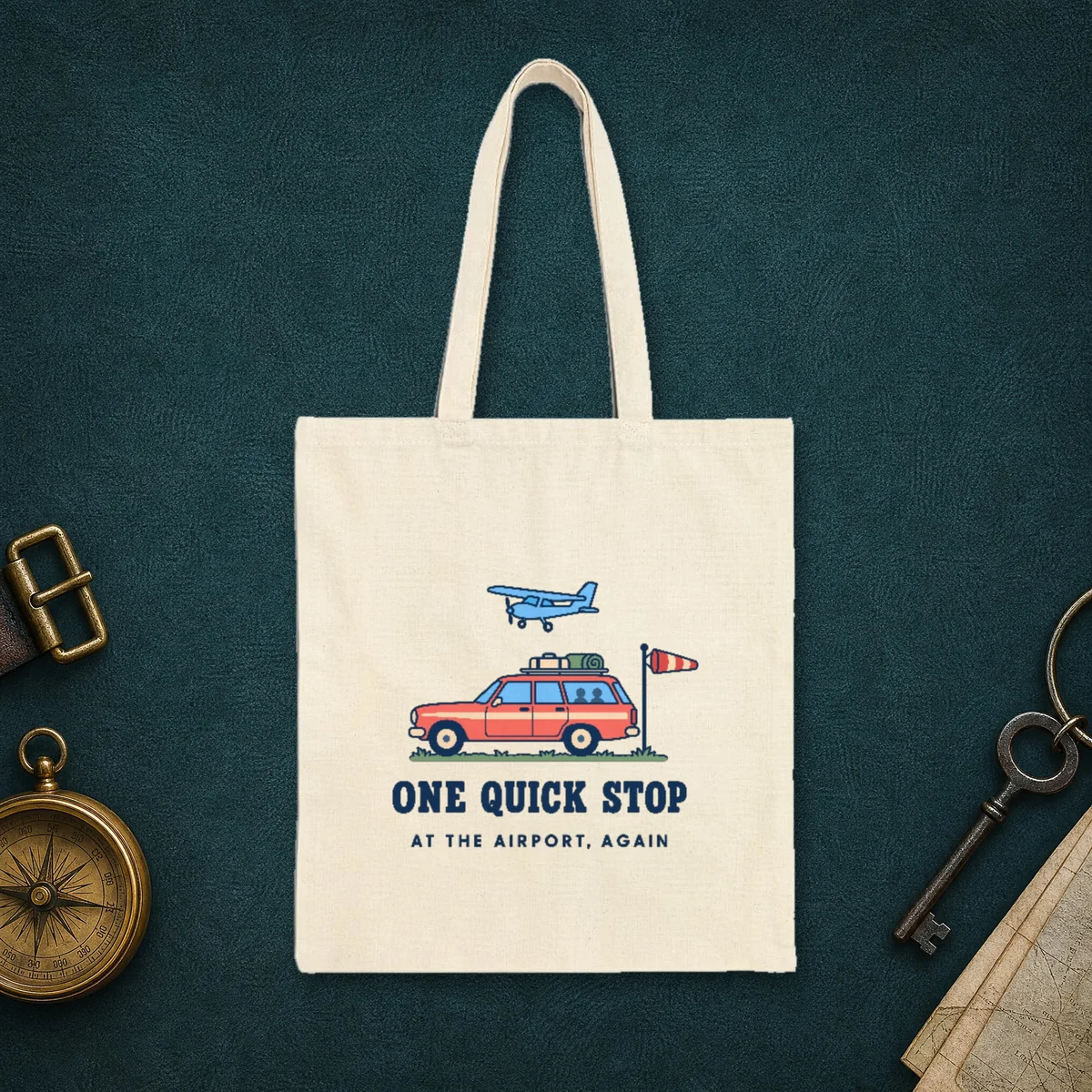 One Quick Stop design in navy ink on a natural canvas tote, laid flat on the leather lid of a travel trunk