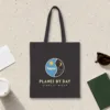 Planes by Day design in warm cream ink on a black canvas tote, laid flat on a light terrazzo terminal floor