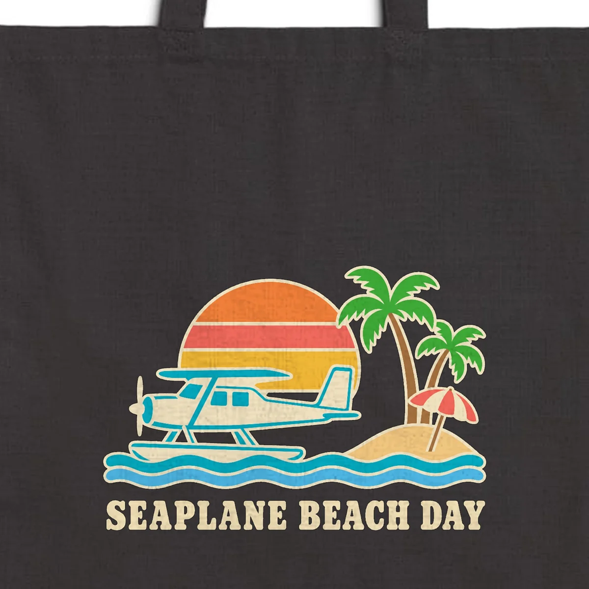 Close-up of the Seaplane Beach Day design printed in warm cream ink on a black canvas tote, with the top seam and handles