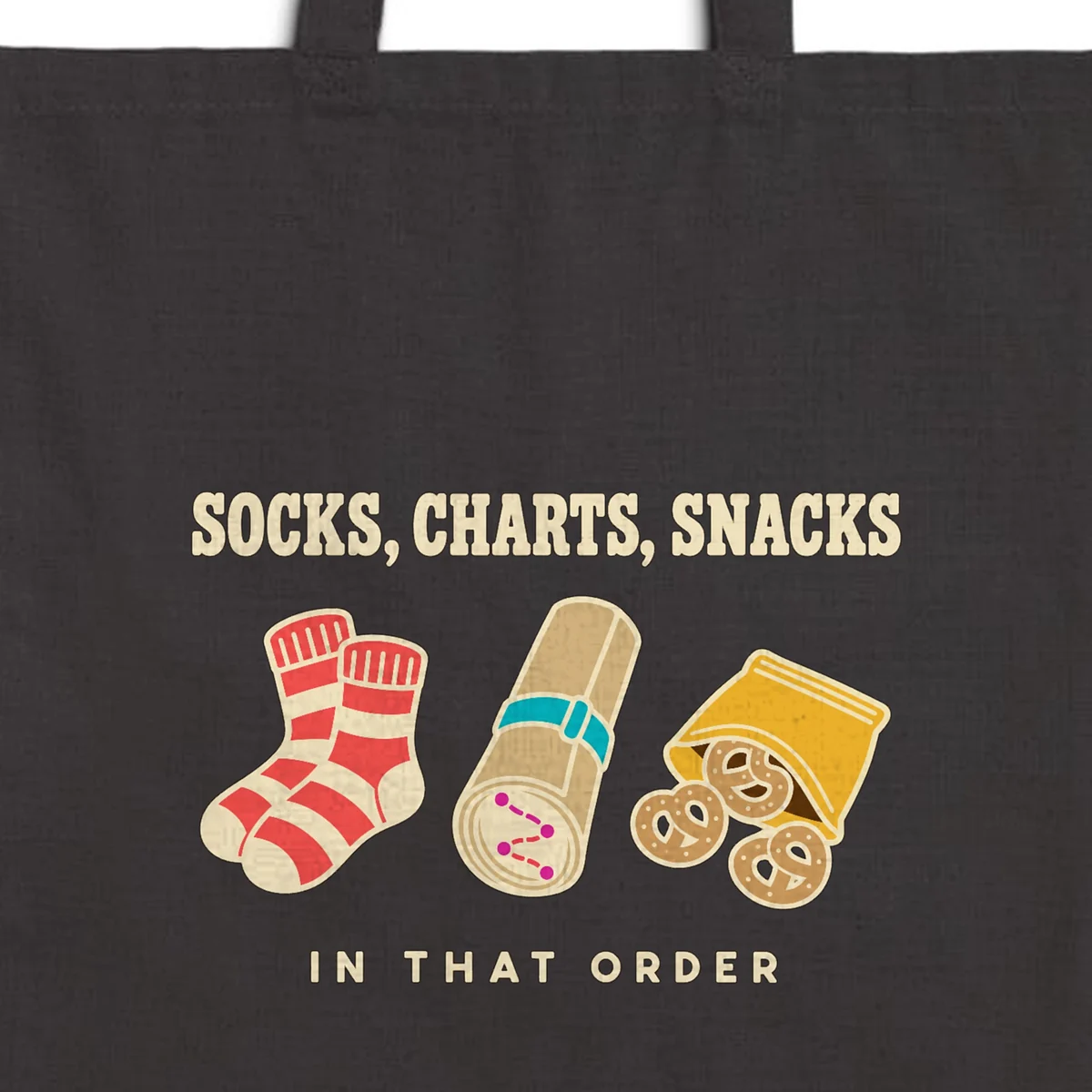 Close-up of the Socks Charts Snacks design printed in warm cream ink on a black canvas tote, with the top seam and handles