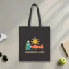 sunshine-and-avgas-tote-black-front Sunshine and Avgas design in warm cream ink on a black canvas tote, laid flat on a sunlit terminal floor by the window