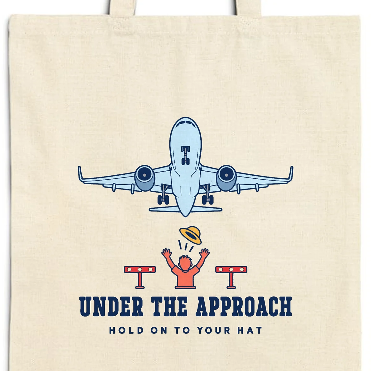 Close-up of the Under the Approach design printed in navy ink on a natural canvas tote, with the top seam and handles
