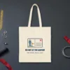 We Met at the Airport design in navy ink on a natural canvas tote, laid flat on a hangar floor