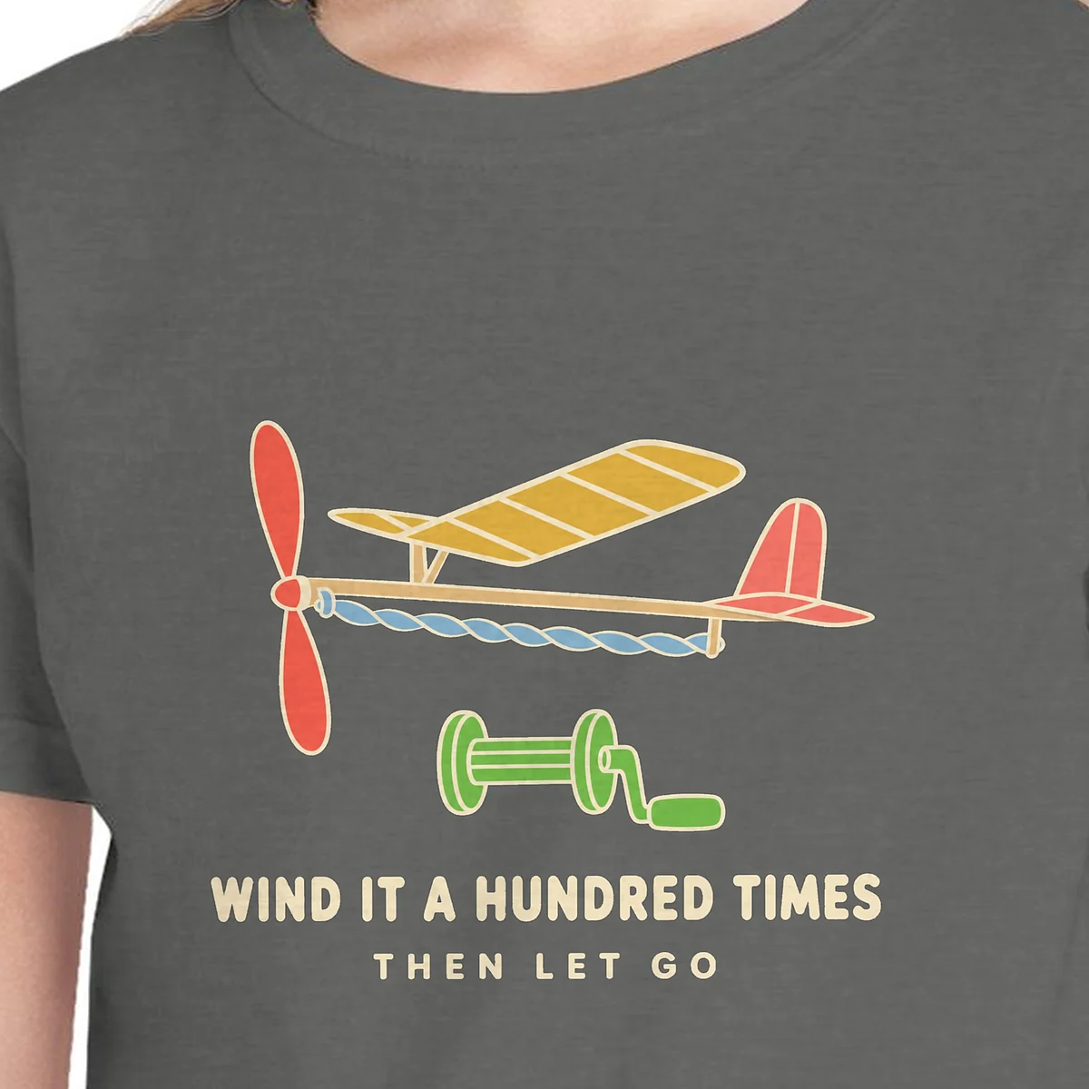 Close-up of the Wind It a Hundred Times design on the Pepper kids tee, Comfort Colors 9018 youth tee, with the neckline