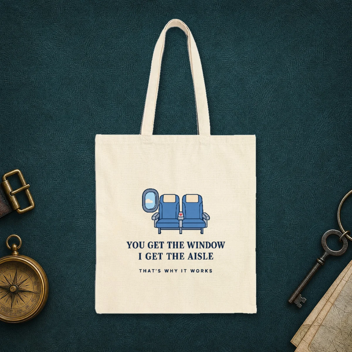 Window and Aisle design in navy ink on a natural canvas tote, laid flat on the leather lid of a travel trunk