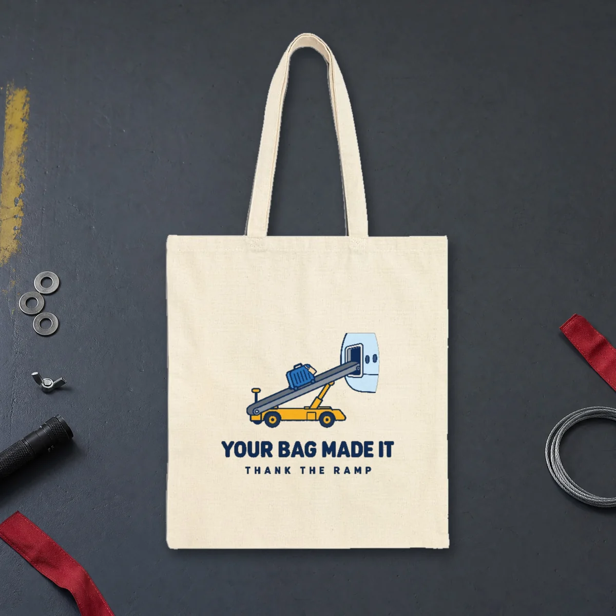 Your Bag Made It design in navy ink on a natural canvas tote, laid flat on a hangar floor